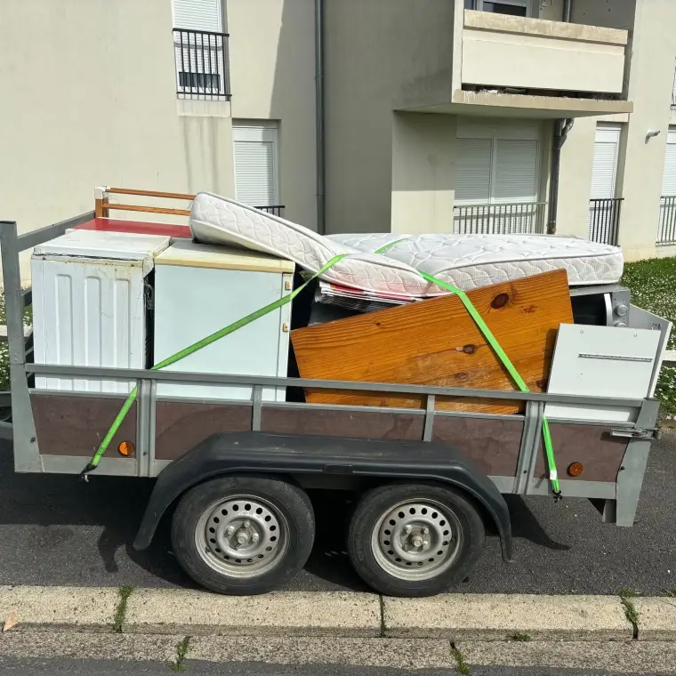 Remorque chargée d’un réfrigérateur, d’un matelas et de mobilier devant un immeuble